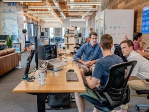 Three men at a table in an office, discussing knowledge sharing initiatives aimed at enhancing employee development and retention.